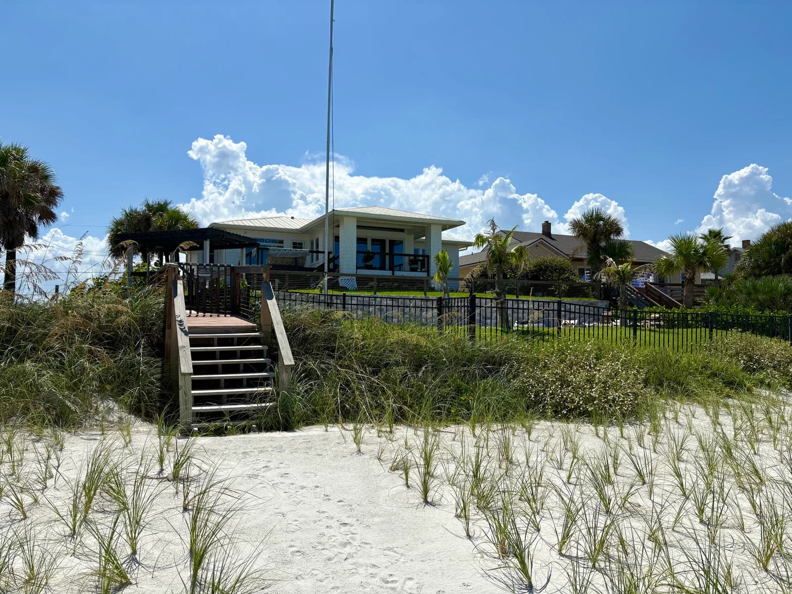 Timber dune walkover and steps rising from the sand through sea oats toward the fenced rear yard