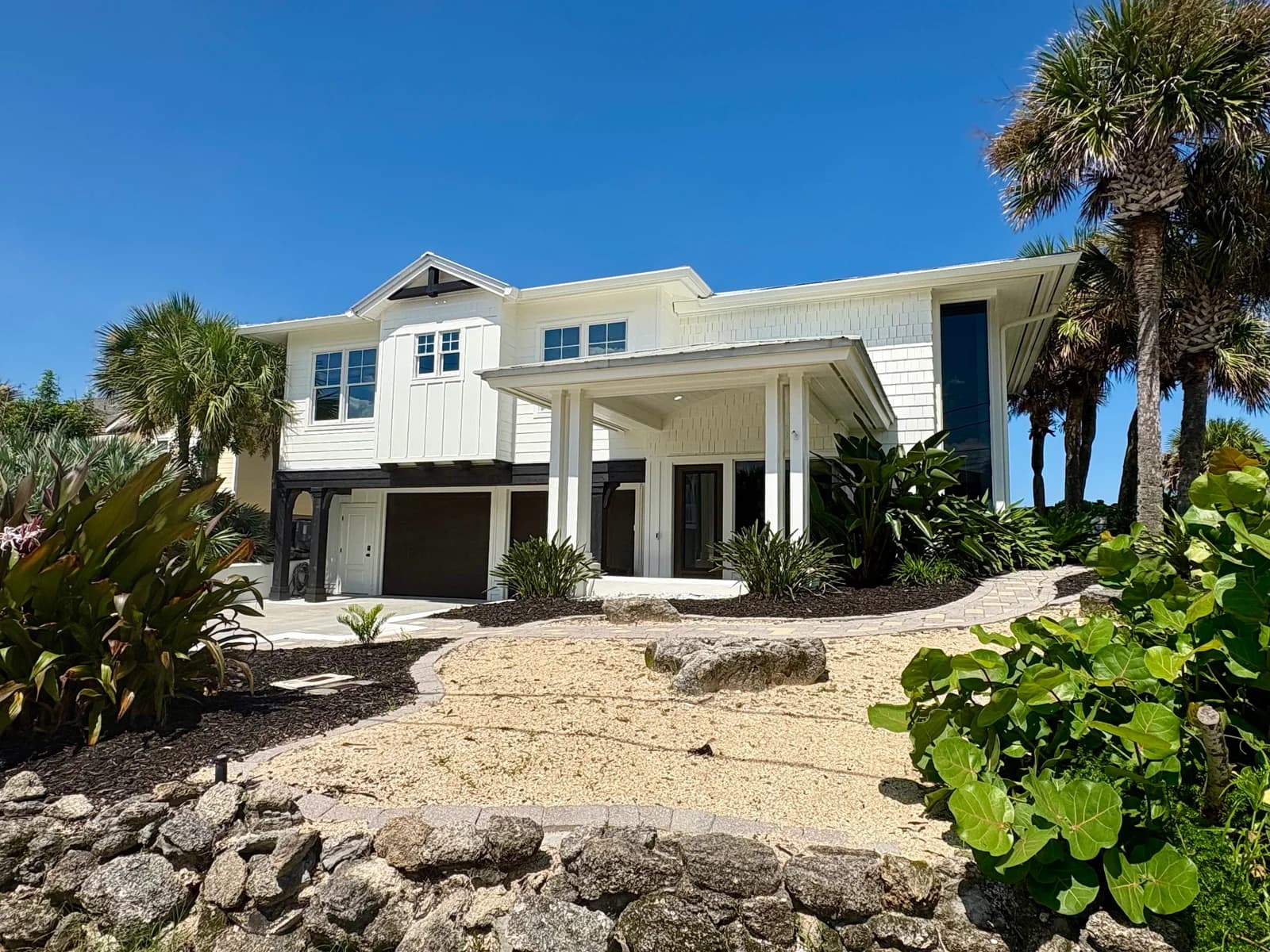 3111 Hill Street from the driveway, a two-storey white coastal residence with a covered entry, metal roof and mature tropical planting